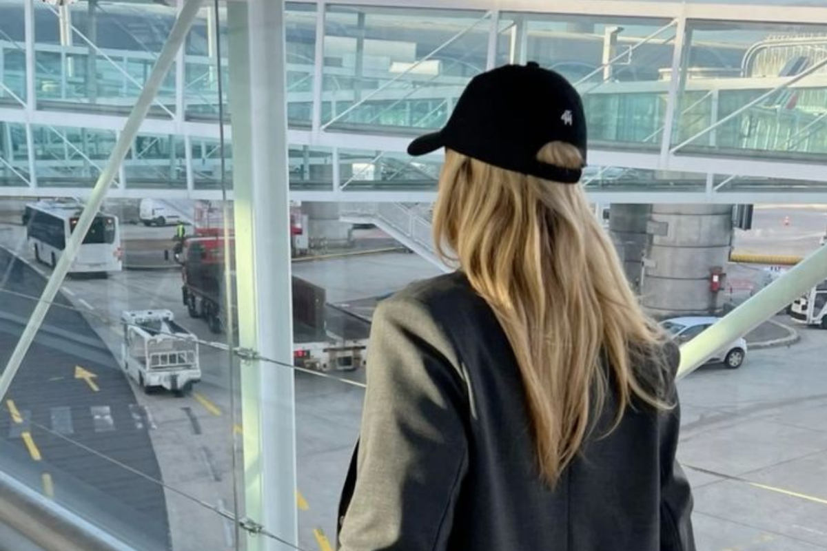 Fashionable blonde girl with long hair boarding a plane wearing a black baseball cap